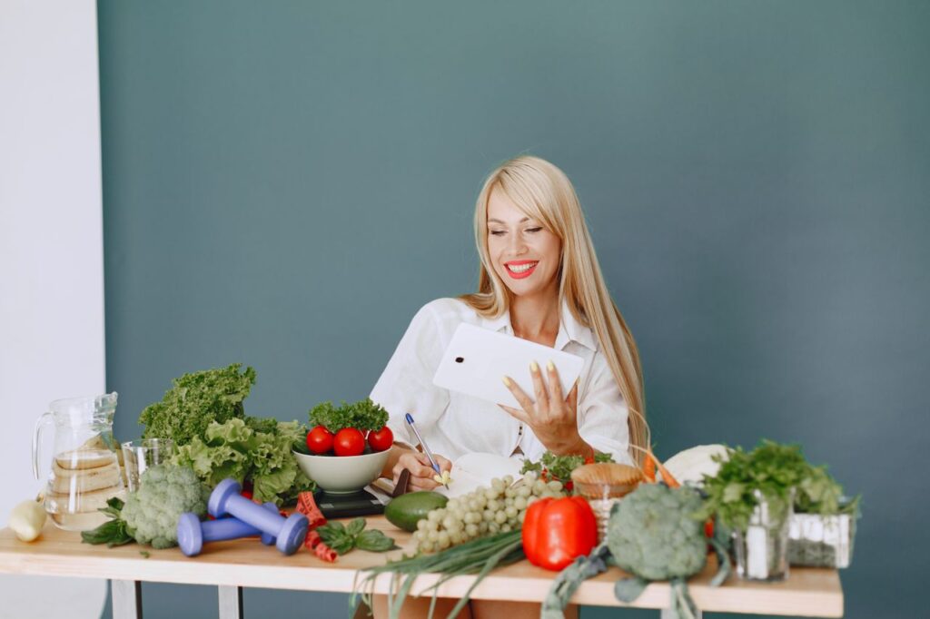 Woman using a tablet surrounded by fresh vegetables at a table, showcasing healthy lifestyle and technology.