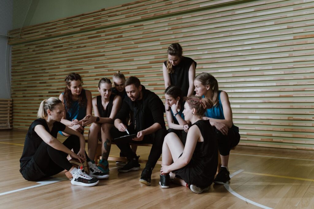 Female basketball team listening to coach's strategy session indoors.